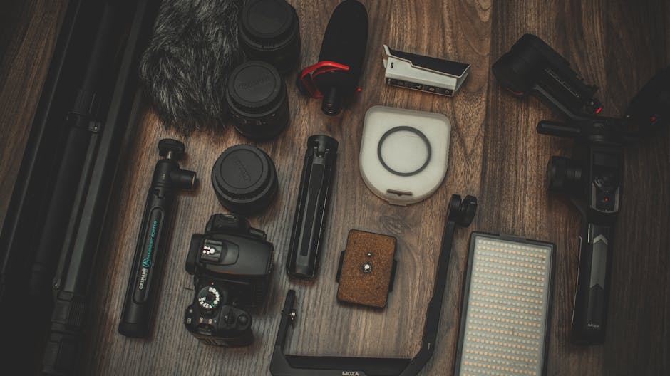 A collection of professional photography gear including a DSLR camera, lenses, and microphone arranged on a wooden surface.