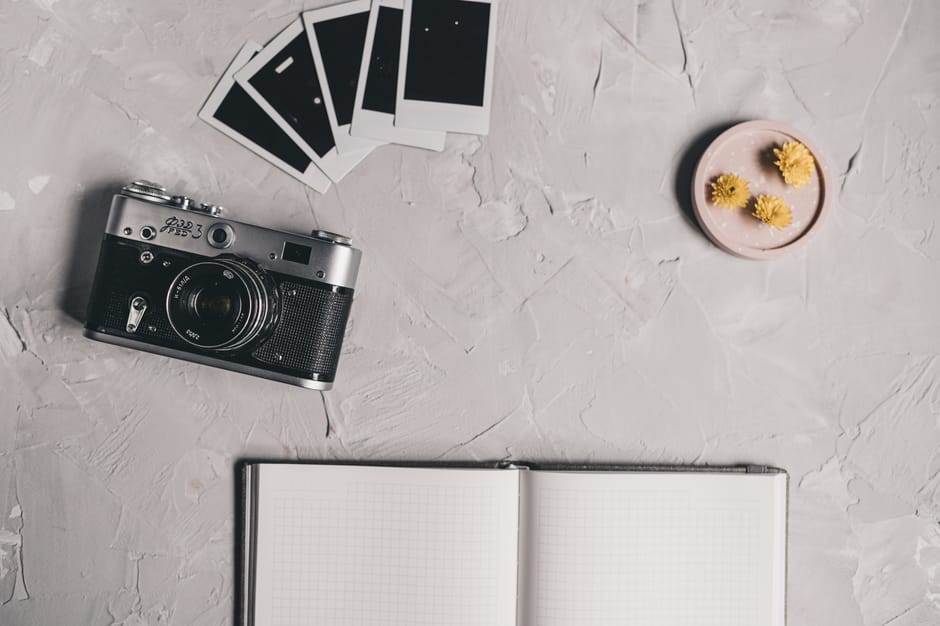 A vintage camera and polaroids on a textured desk with an open notebook and flowers.